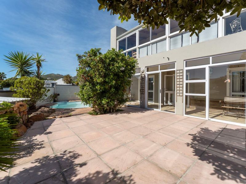Rear exterior view featuring a paved patio area, a small swimming pool, and large glass sliding doors leading into the apartment.