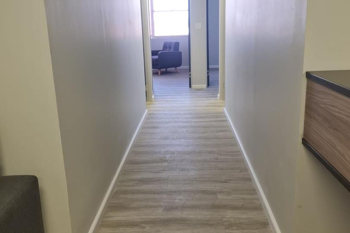 A clean, well-lit office hallway featuring modern wood-look vinyl flooring, neutral walls, and a drop ceiling with integrated lighting.
