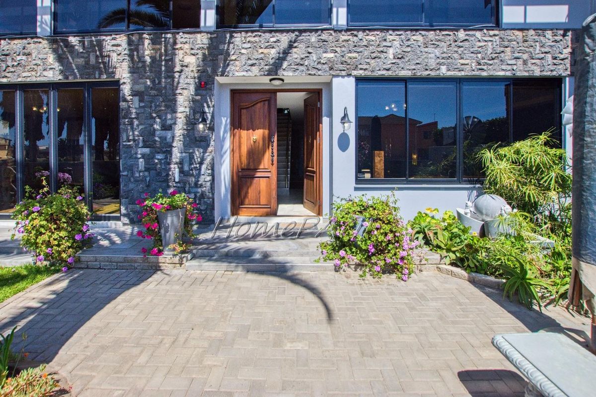 Rear exterior view featuring a paved patio area, stone-clad facade, and a prominent double timber entrance door with large aluminium-framed windows.