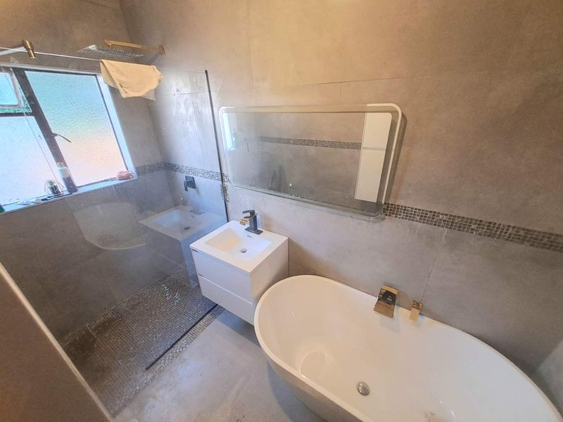 Modern bathroom featuring a freestanding bathtub, glass-enclosed shower, wall-mounted vanity with basin, and neutral tiled walls with mosaic accents.