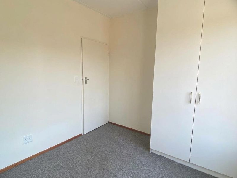 A clean, empty bedroom featuring neutral walls, grey carpet flooring, and a built-in wardrobe with modern handles.