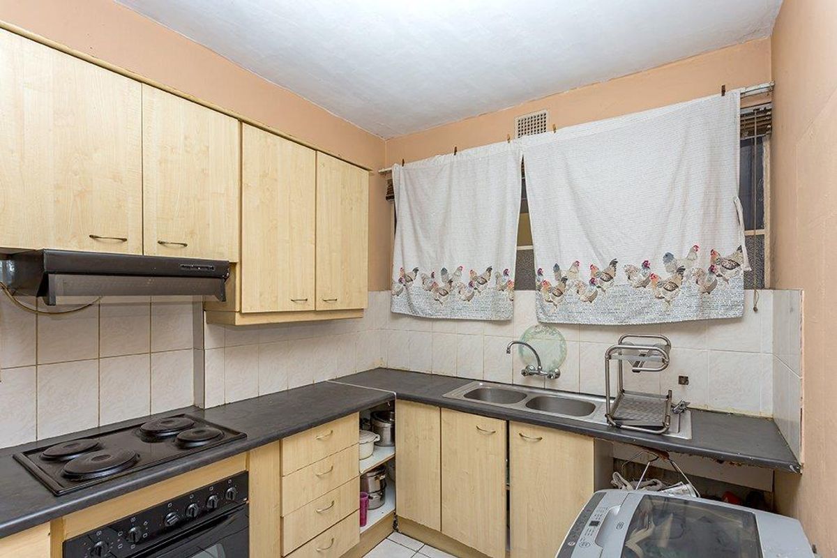 A compact kitchen featuring light wood-tone cabinetry, a double stainless steel sink, and built-in electric cooking appliances with a tiled backsplash.