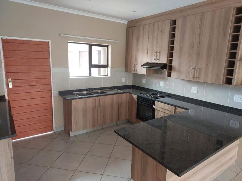 A functional kitchen featuring wood-finish cabinetry, granite countertops, a built-in oven with hob, and tiled flooring, offering a clean and practical workspace.