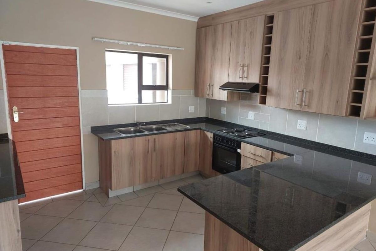 A functional kitchen featuring wood-finish cabinetry, granite countertops, a built-in oven with hob, and tiled flooring, offering a clean and practical workspace.