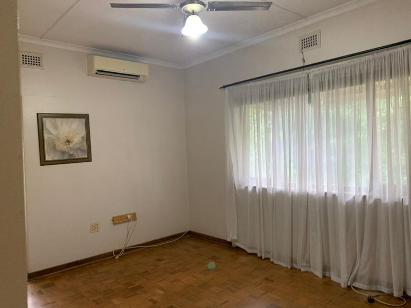 A bright, empty bedroom featuring classic parquet flooring, a ceiling fan, and a wall-mounted air conditioning unit.