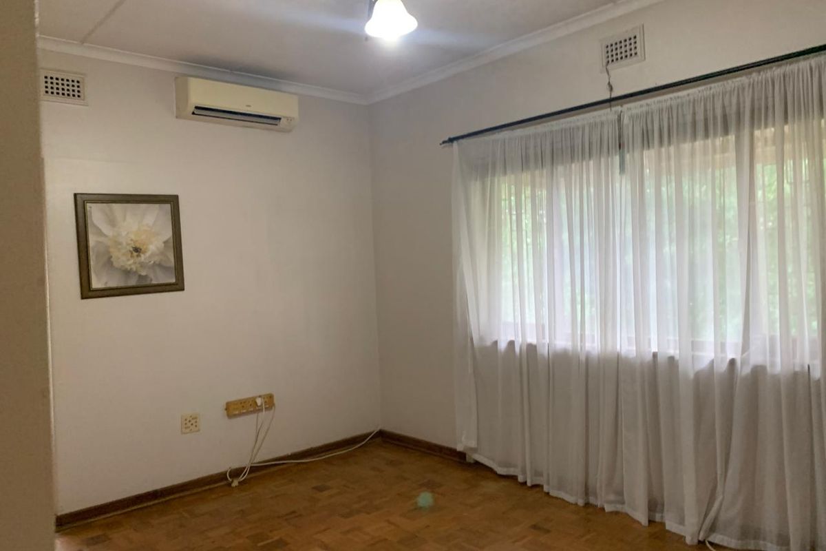 A bright, empty bedroom featuring classic parquet flooring, a ceiling fan, and a wall-mounted air conditioning unit.