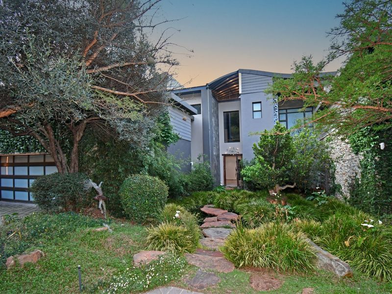A modern architectural home exterior featuring stone cladding, a landscaped garden with a stone pathway, and a contemporary garage door.