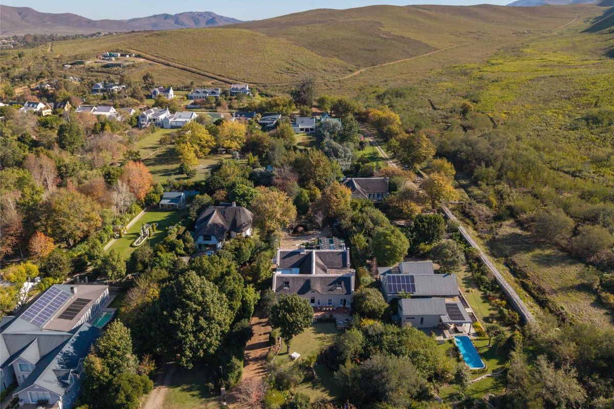 Aerial view of a residential estate featuring multiple homes with thatched roofs, solar installations, swimming pools, and expansive landscaped gardens in a scenic setting.