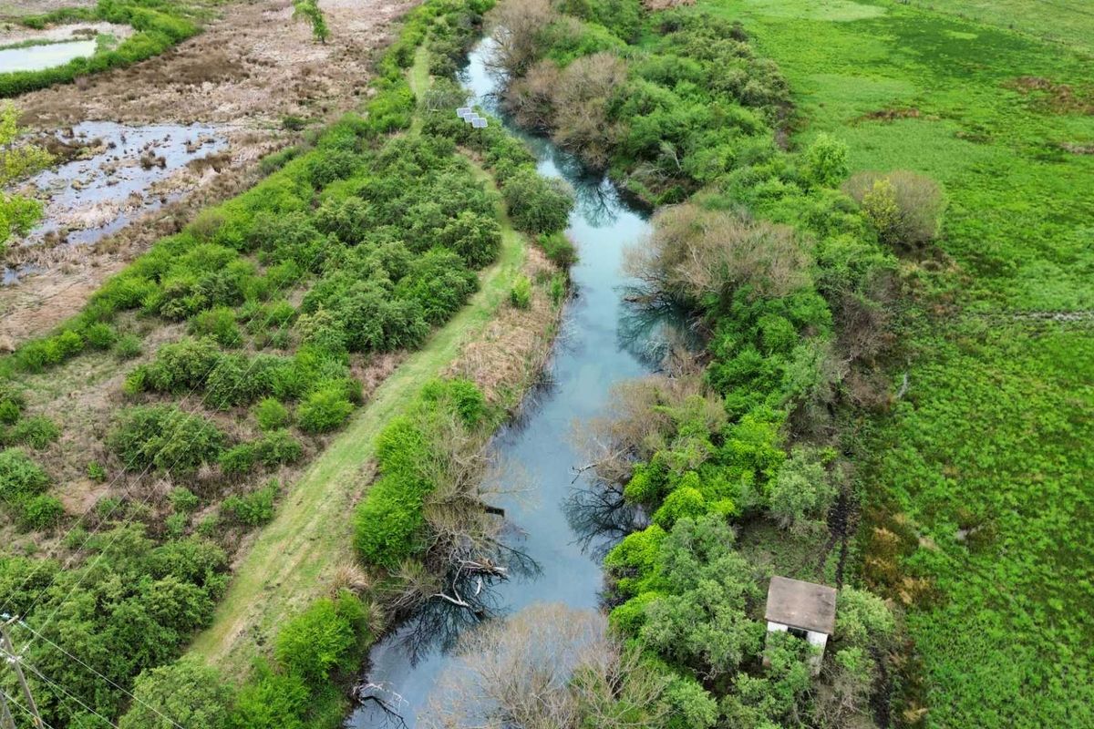 An aerial view of a natural river landscape surrounded by lush green vegetation and open fields.
