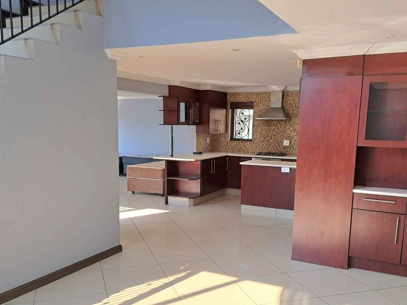 Open plan kitchen featuring dark wood cabinetry, mosaic backsplash, and integrated appliances, seamlessly connected to the living area and staircase.