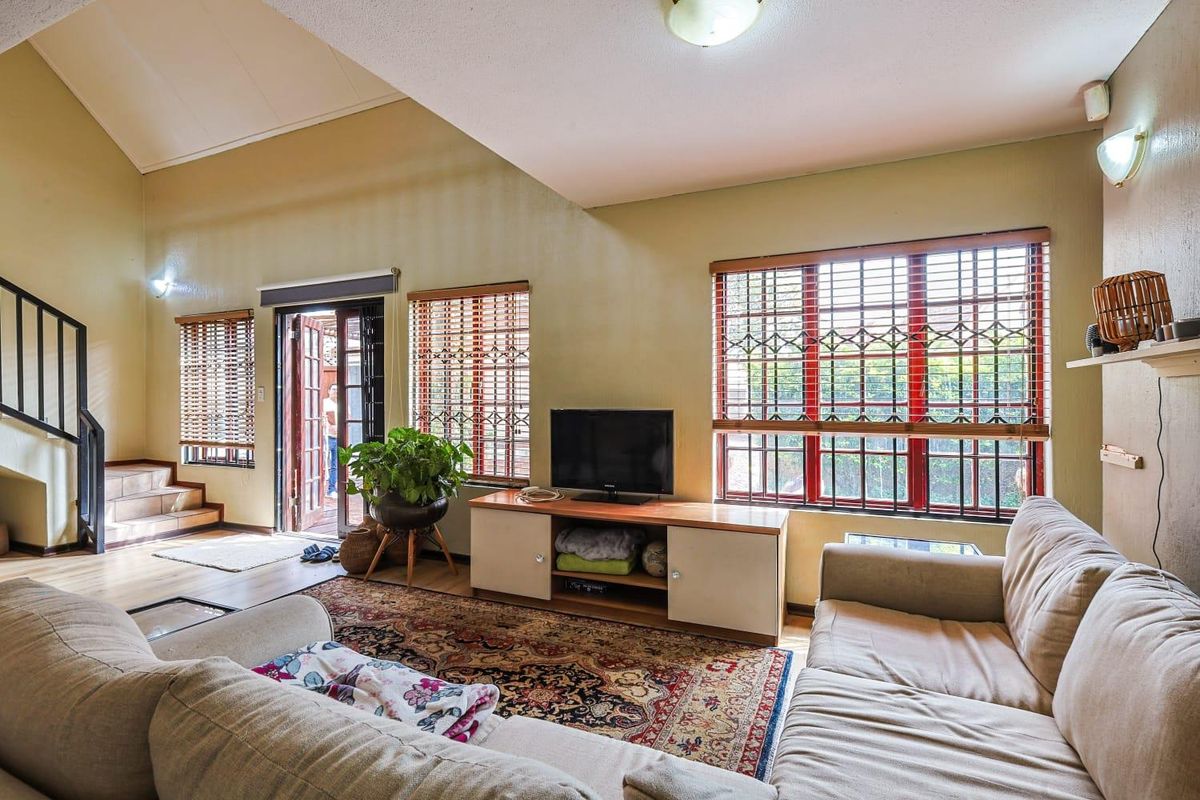 Spacious living room featuring high vaulted ceilings, large windows with security bars, and direct access to an outdoor patio area.