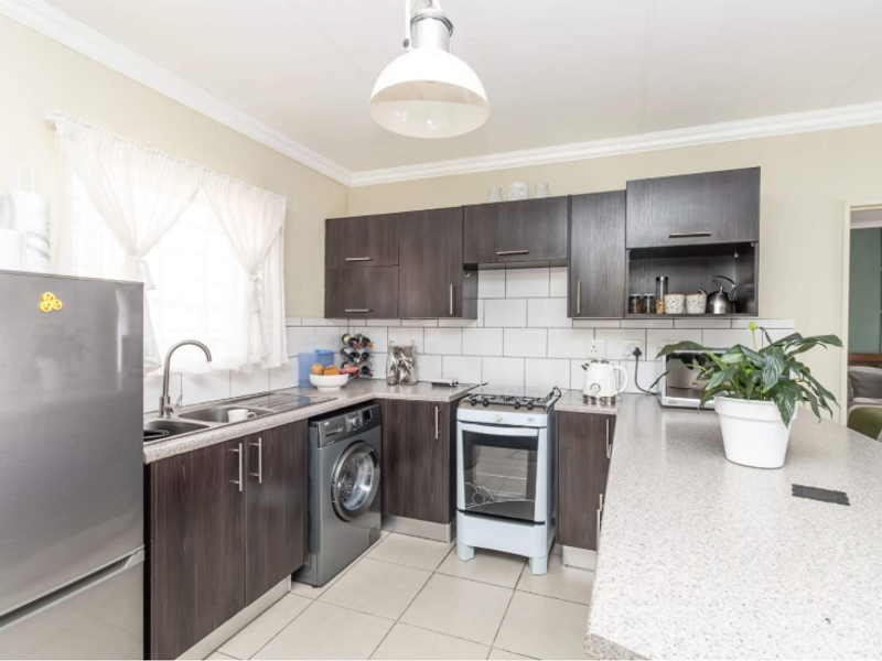 A functional kitchen featuring dark wood cabinetry, light laminate countertops, a tiled backsplash, and integrated laundry facilities, offering a clean and practical workspace.