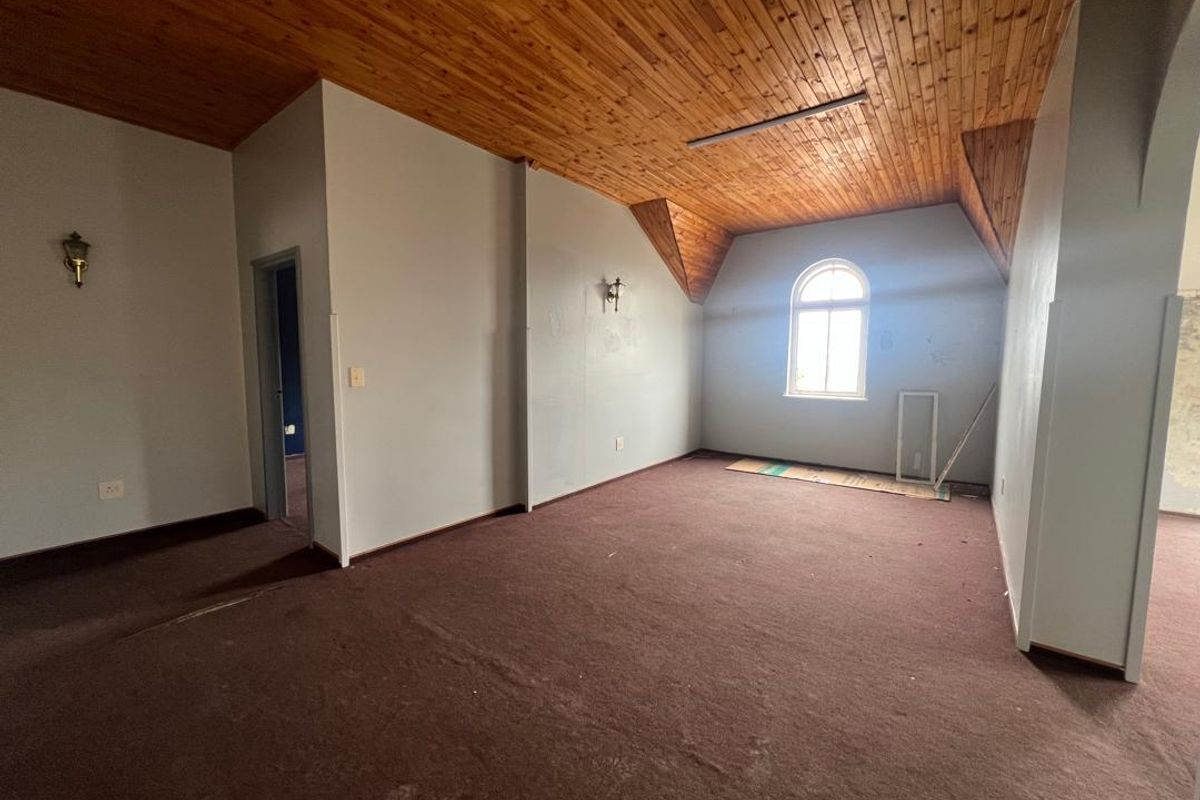 Spacious interior room featuring a vaulted timber ceiling, arched window, and wall-mounted lighting fixtures, currently presented as an empty, versatile space.