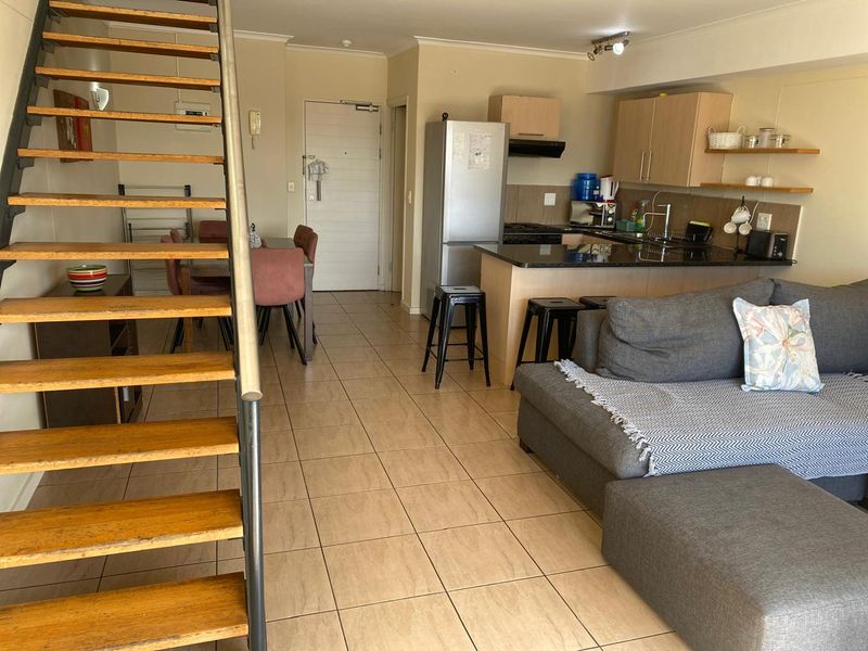 Open-plan living area featuring a kitchen with granite countertops, tiled flooring, and a staircase leading to the upper level.