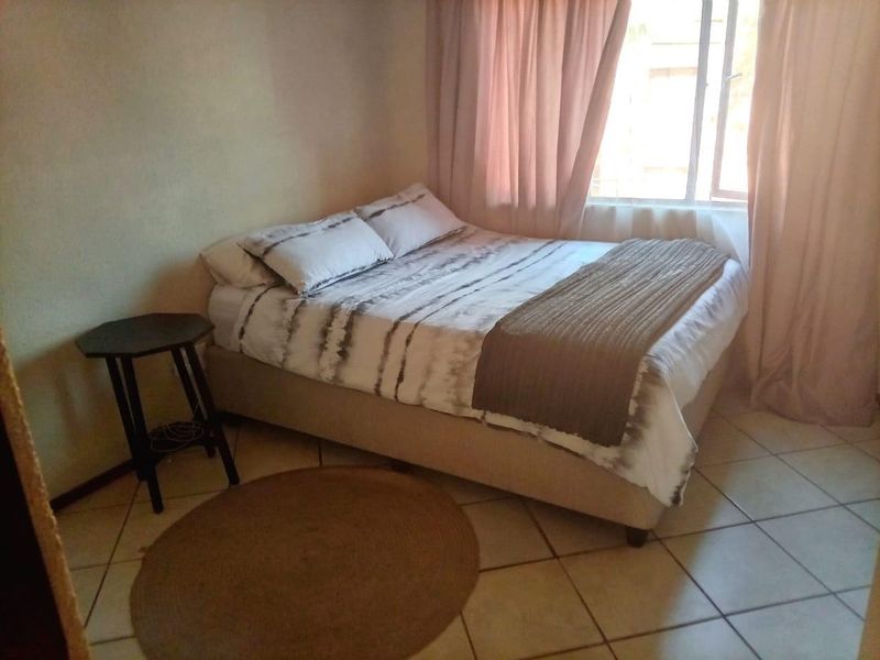 A functional bedroom featuring tiled flooring and a window with curtains, providing a simple and practical living space.