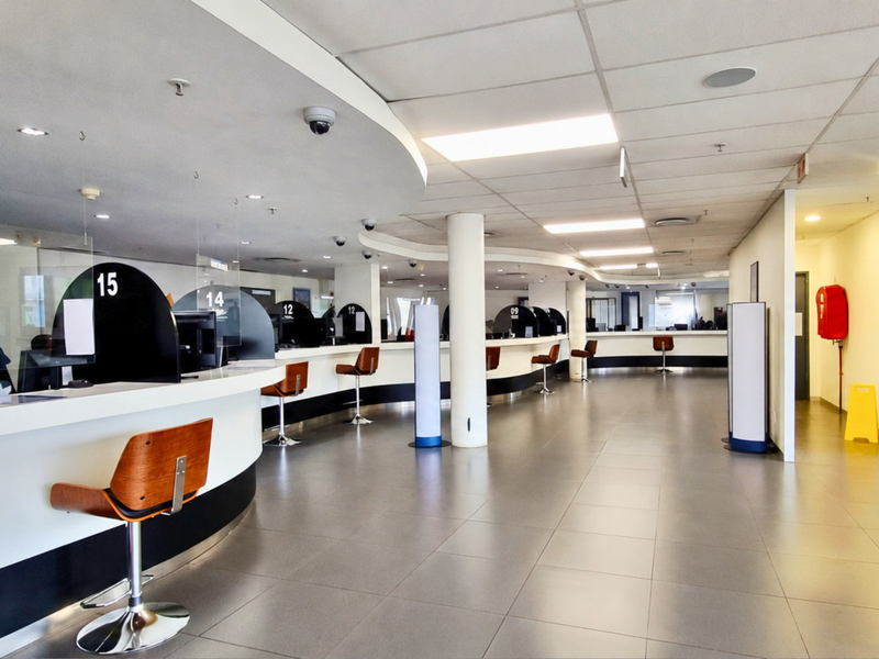 A modern, well-maintained office reception and service area featuring long curved counters, tiled floors, and integrated security and lighting systems.