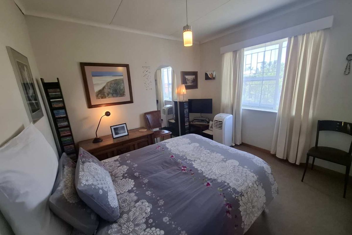 A standard bedroom featuring neutral walls, carpeted flooring, and a window fitted with security bars and curtains.