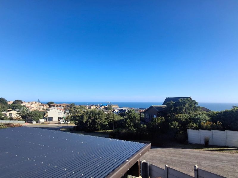 Elevated coastal view overlooking the surrounding neighbourhood and ocean horizon, captured from an upper level with a corrugated metal roof in the foreground.