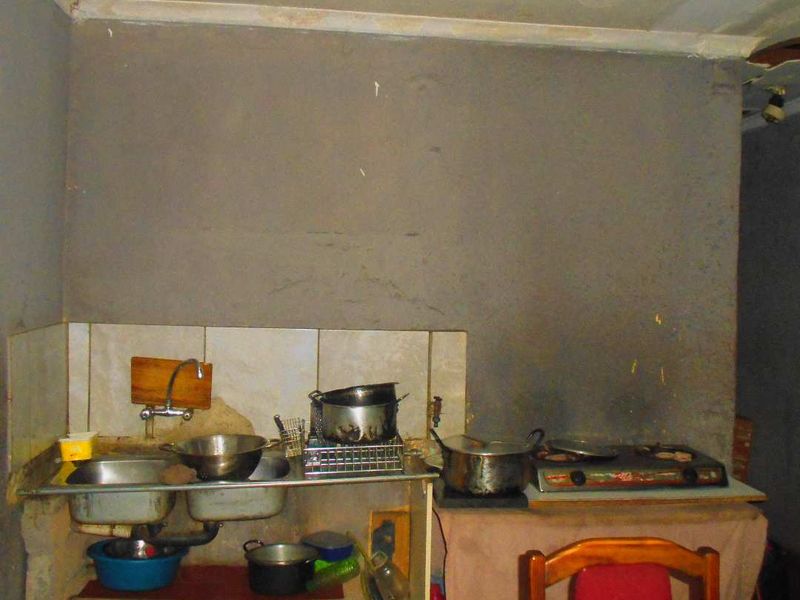 A basic kitchen area featuring a stainless steel double sink and tiled splashback, currently requiring significant renovation and repair to wall and ceiling finishes.