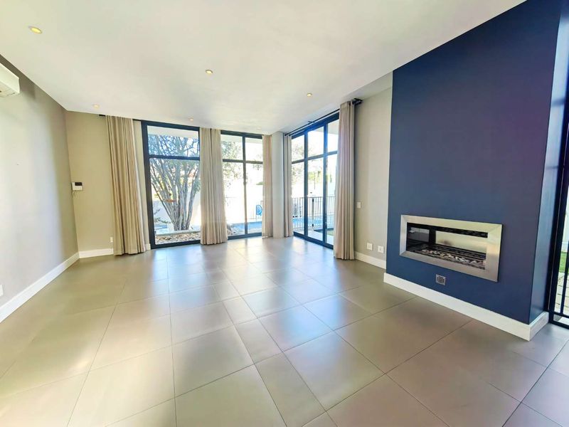 Spacious, modern living room featuring large windows, tiled flooring, and a sleek built-in fireplace, offering a bright and open atmosphere.
