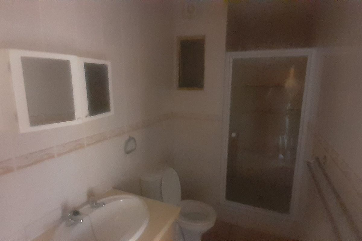 A compact bathroom featuring a shower enclosure, vanity basin, and toilet, requiring modernization to improve functionality and aesthetic appeal.