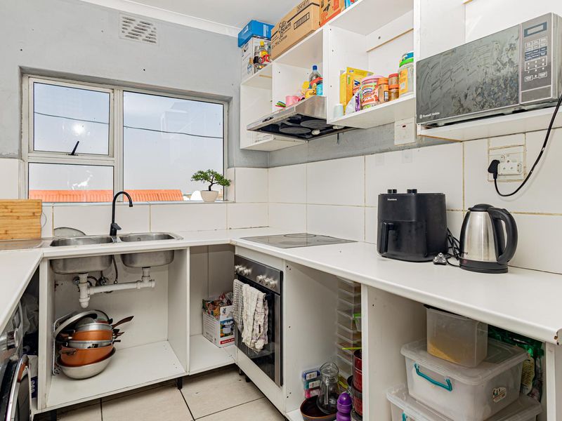 Compact kitchen featuring a double sink, built-in oven, electric hob, and open shelving, requiring cosmetic updates and cabinet door installation.