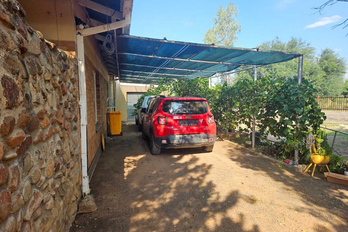 Rear exterior area featuring a stone-clad wall and a shaded carport structure over an unpaved driveway.