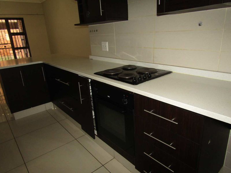A clean, modern kitchen featuring dark wood cabinetry, stone countertops, a built-in oven, and an electric hob with a tiled backsplash.