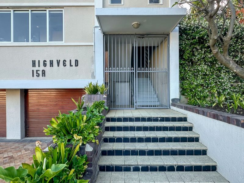 Front entrance of the apartment building featuring a secure metal gate, tiled staircase, and integrated brick planter boxes.