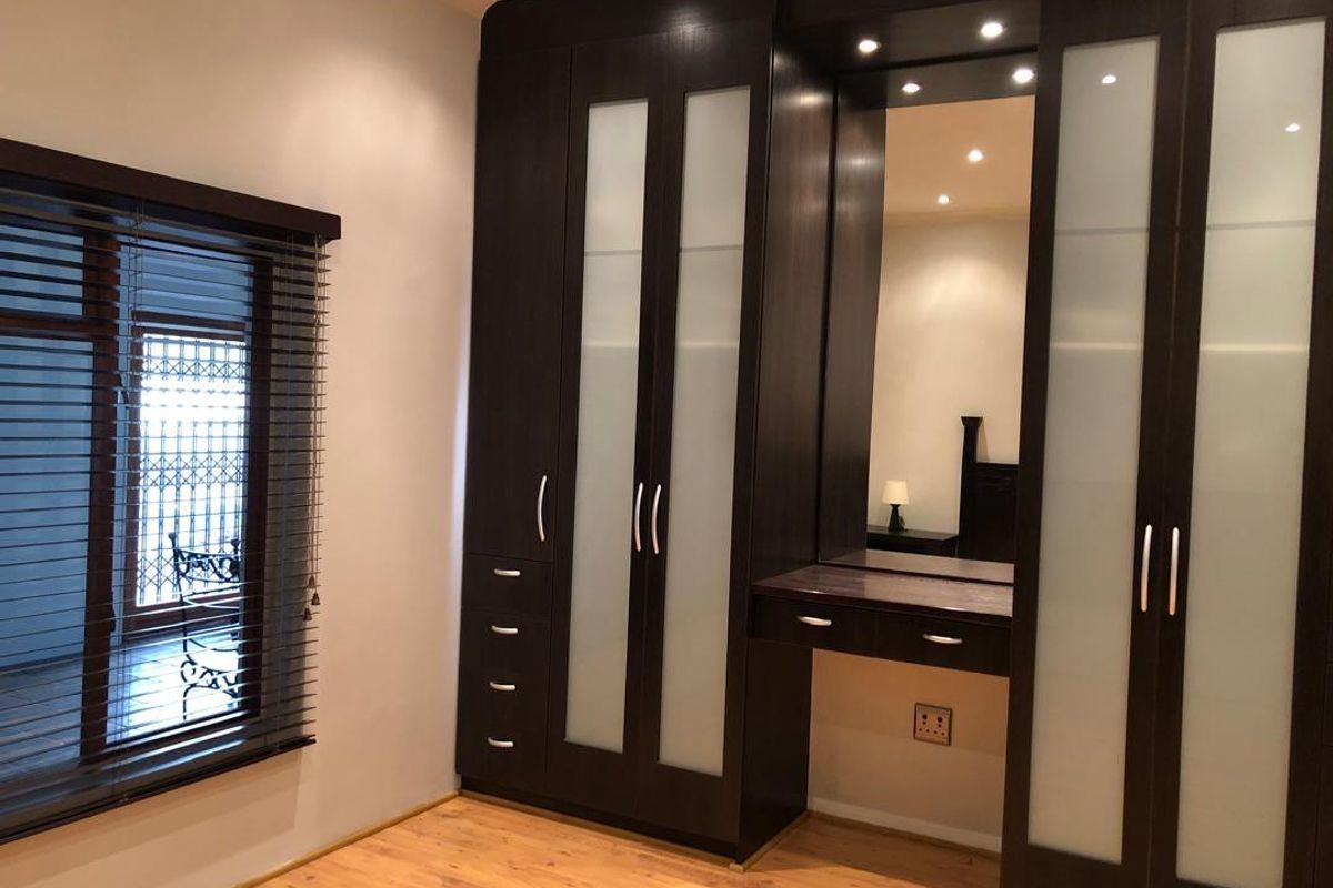 A bedroom featuring dark wood built-in cupboards with frosted glass panels, an integrated vanity area, laminate flooring, and venetian blinds.