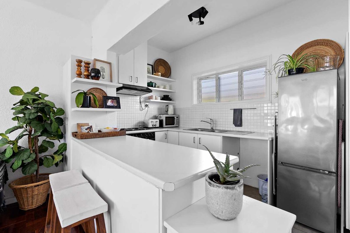 A bright, functional kitchen featuring white cabinetry, tiled backsplash, integrated hob and oven, and a convenient breakfast bar counter.
