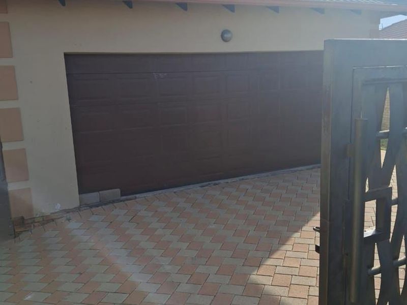 Front view of the property featuring a paved driveway, a brown garage door, and a secure metal gate entrance.