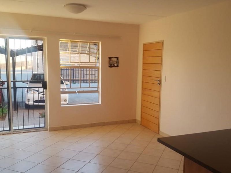 An open-plan living area featuring tiled flooring, a sliding glass door with security gate, and a wooden interior door.
