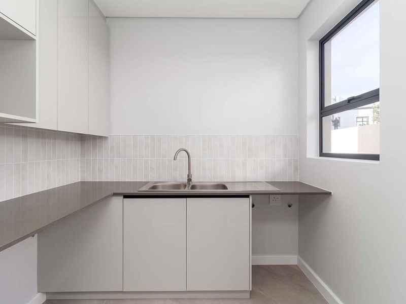 A clean, modern laundry room featuring built-in cabinetry, a stainless steel sink, and dedicated plumbing connections for appliances.