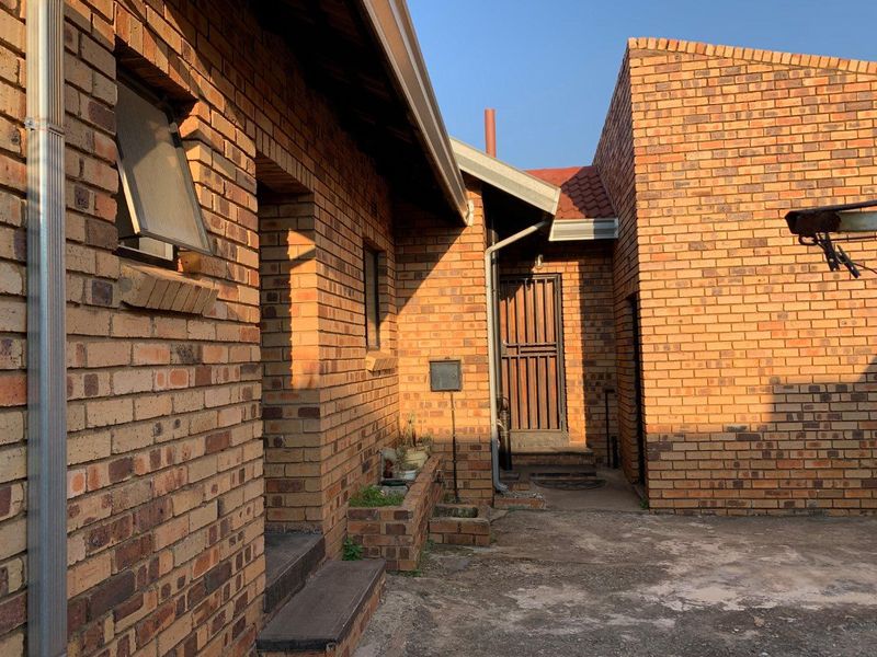 A rear exterior view of the property featuring face brick walls, a security gate, and a concrete paved courtyard area.