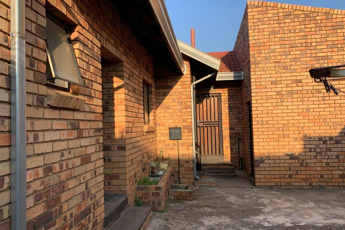 A rear exterior view of the property featuring face brick walls, a security gate, and a concrete paved courtyard area.
