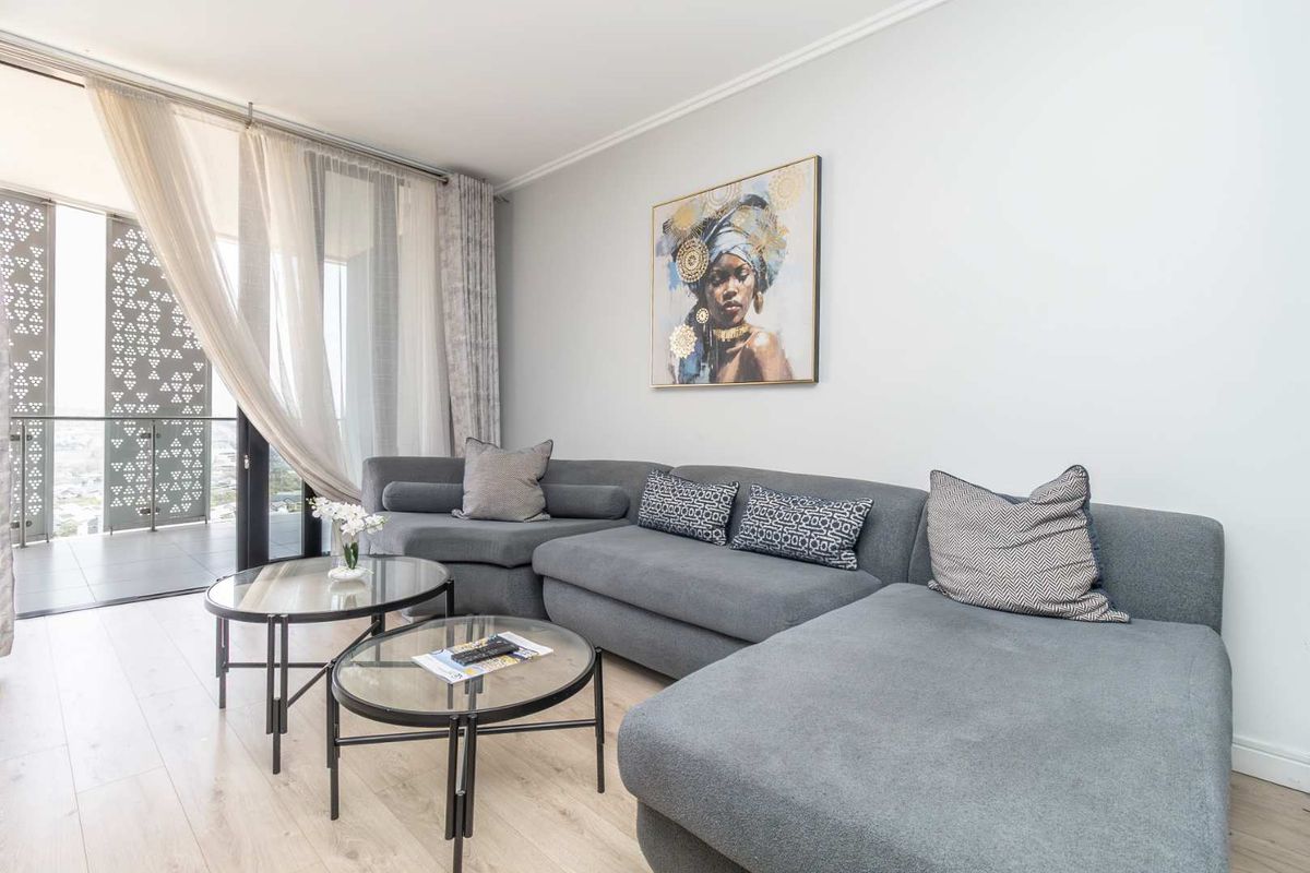 A bright and modern living room featuring light laminate flooring and a large sliding glass door leading to a balcony with a decorative screen.