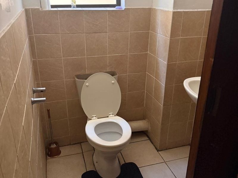 A functional bathroom featuring a standard toilet, pedestal basin, and neutral ceramic tiling throughout.