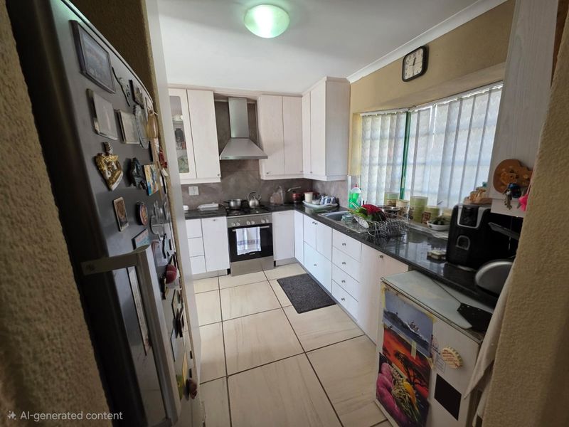 A functional kitchen featuring light-toned cabinetry, granite countertops, a stainless steel extractor fan, and tiled flooring with a practical layout.