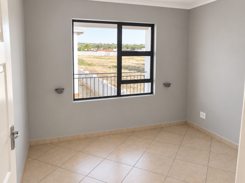 A bright, empty bedroom featuring neutral grey walls, tiled flooring, and a large aluminium-framed window with a view of the surrounding area.