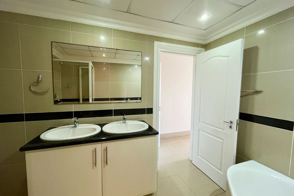 A functional bathroom featuring a double vanity with granite countertop, neutral wall tiling with a decorative border, and recessed ceiling lighting.