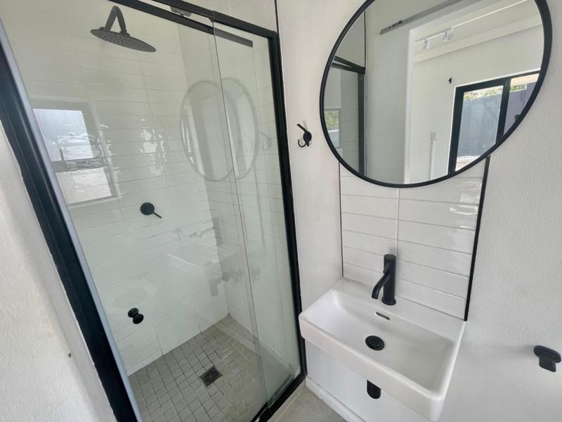 Modern bathroom featuring a walk-in shower with black framed glass, a wall-mounted basin with black fixtures, and a contemporary round mirror.