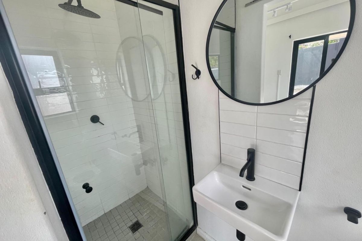 Modern bathroom featuring a walk-in shower with black framed glass, a wall-mounted basin with black fixtures, and a contemporary round mirror.