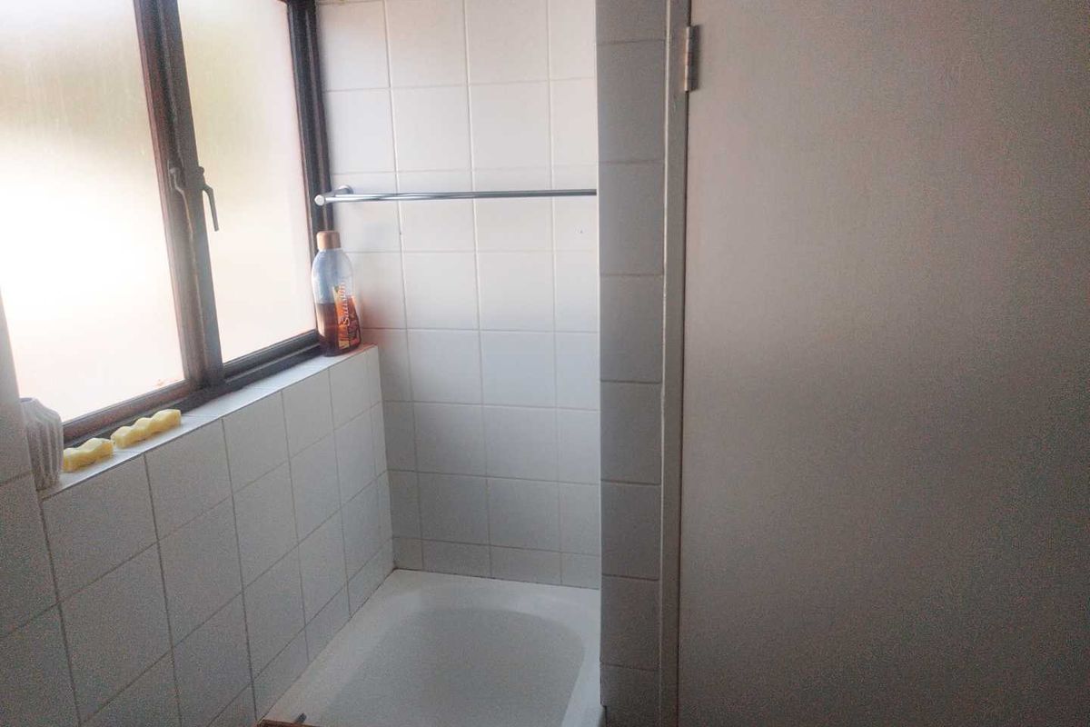 A compact bathroom featuring a built-in shower area with white wall tiles, a window, and a chrome towel rail.