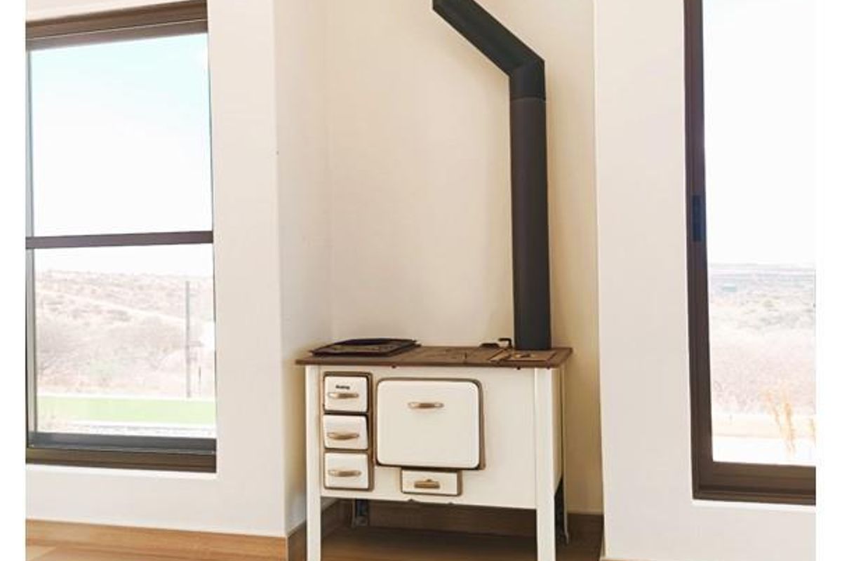 A bright living area featuring a vintage-style wood-burning stove with a black flue, set against white walls and light wood-look flooring.