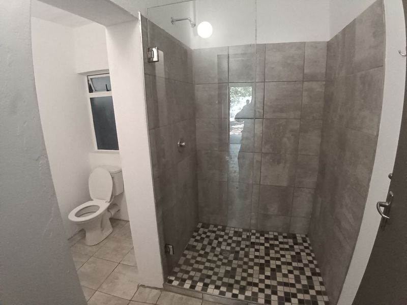 A clean, modern bathroom featuring a walk-in shower with a glass screen, tiled flooring, and a separate toilet area.