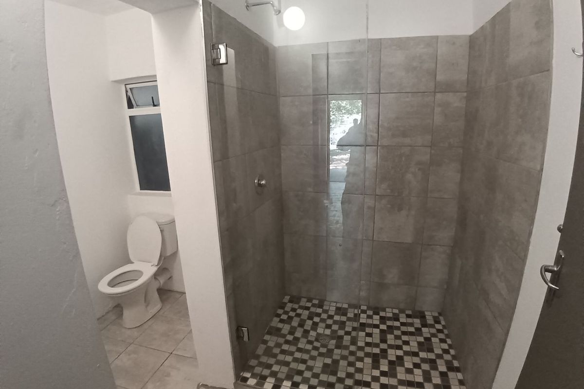 A clean, modern bathroom featuring a walk-in shower with a glass screen, tiled flooring, and a separate toilet area.