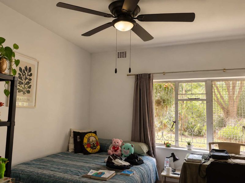 A bedroom featuring a ceiling fan, metal security bars on the window, and neutral wall finishes.