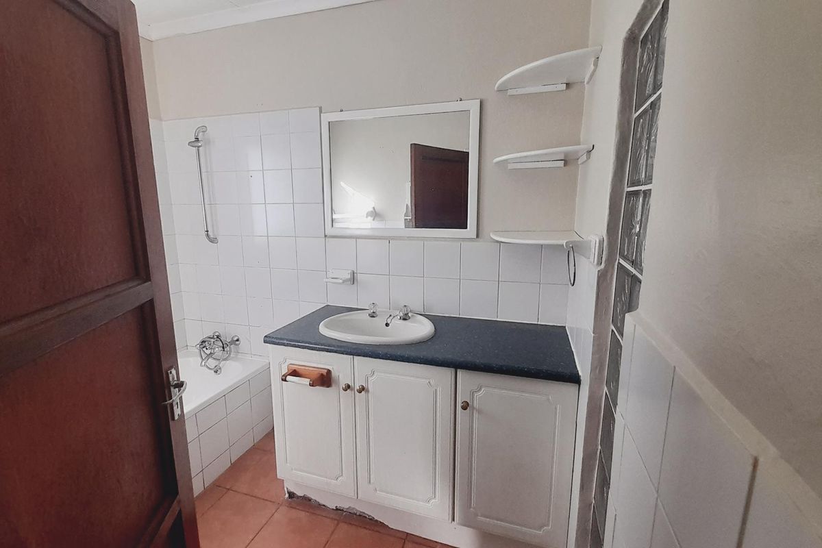 A functional bathroom featuring a built-in vanity with a basin, a bathtub with shower mixer, and glass block feature wall.