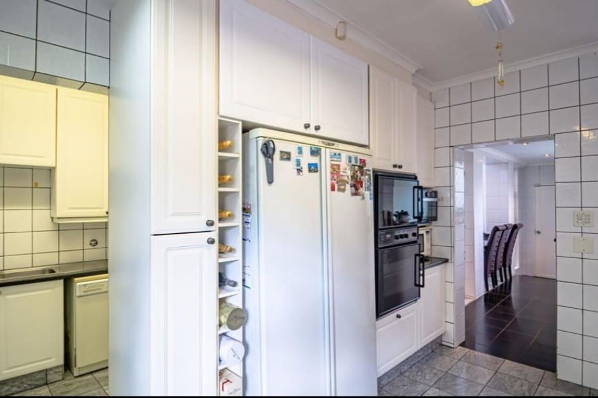 A functional kitchen featuring white cabinetry, a double wall oven, tiled splashbacks, and tiled flooring, with an adjacent dining area visible through the doorway.